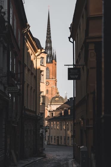 Smal gränd i Gamla stan, Stockholm, med kyrkspiror och äldre byggnader i bakgrunden.