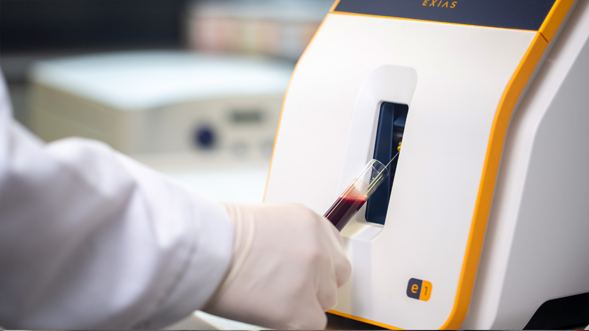 Handske iført hånd indsætter et blodprøverør i et laboratorieanalysemaskine.