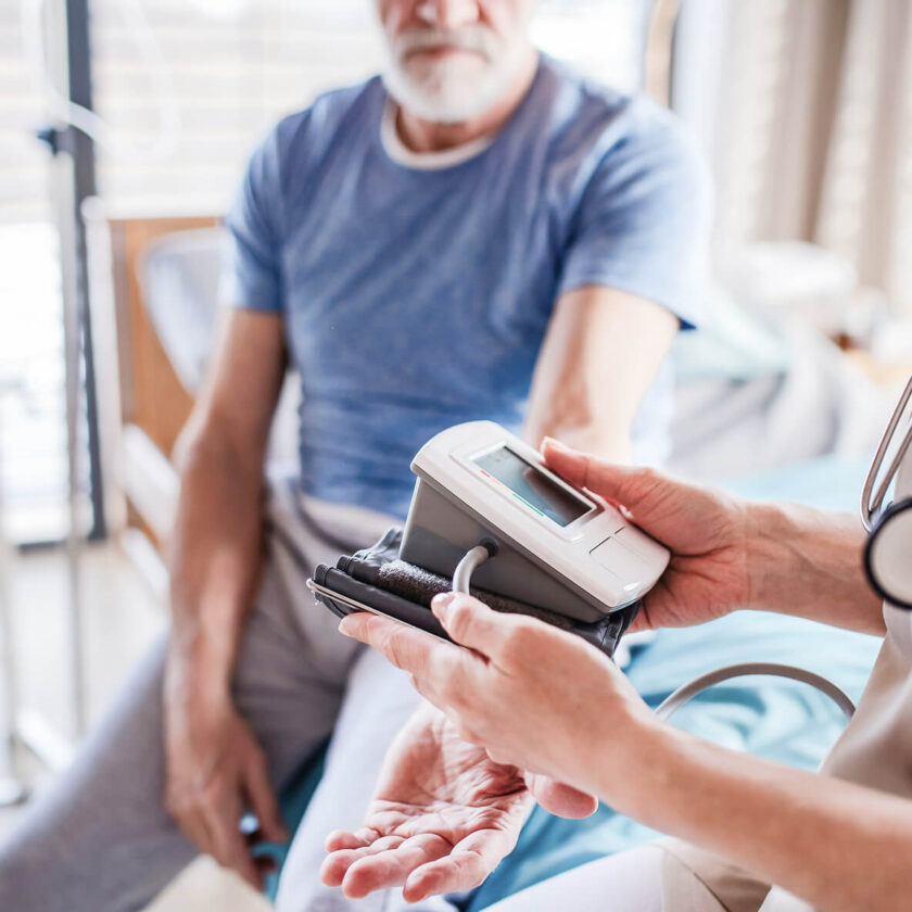 Ældre mand får målt blodtryk med digital blodtryksmåler af sundhedspersonale.