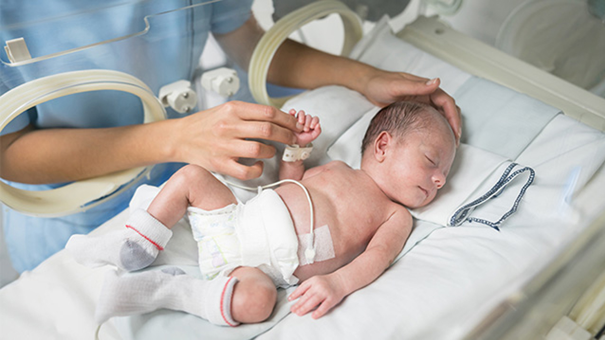 For tidligt født baby ligger i kuvøse på hospitalet, mens en sygeplejerske passer barnet.