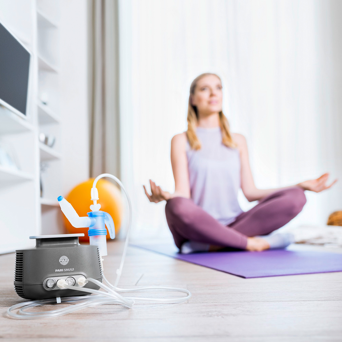 En kvinde sidder med krydsede ben på en yogamåtte, med en forstøverapparat i forgrunden.