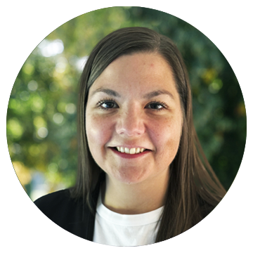 Kvinde med langt, brunt hår smiler foran grøn sløret baggrund.