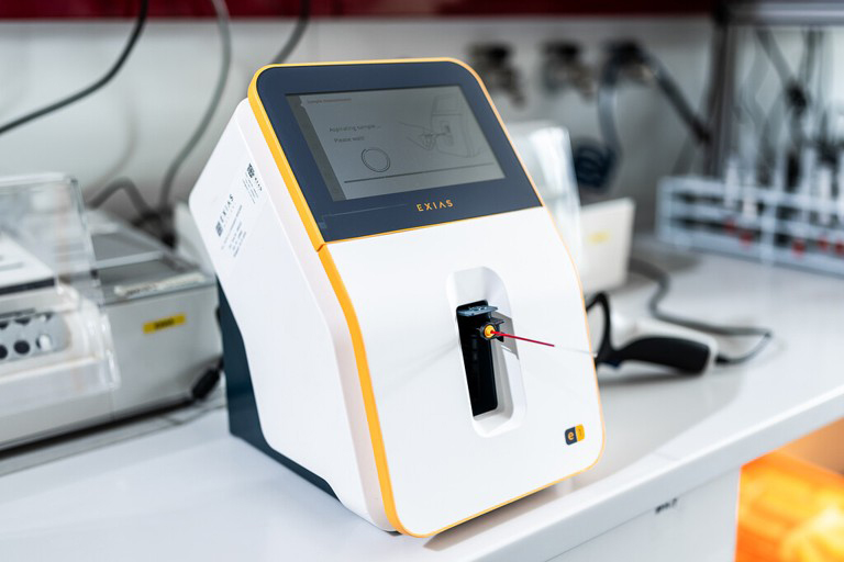 Medicinsk analyseapparat med touchscreen står på et laboratoriebord, én ledning er tilsluttet fronten.