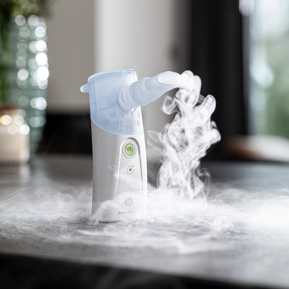 En medicinsk nebulisator, der frigiver synlig tåge, placeret på et bord i et godt oplyst indendørs miljø.